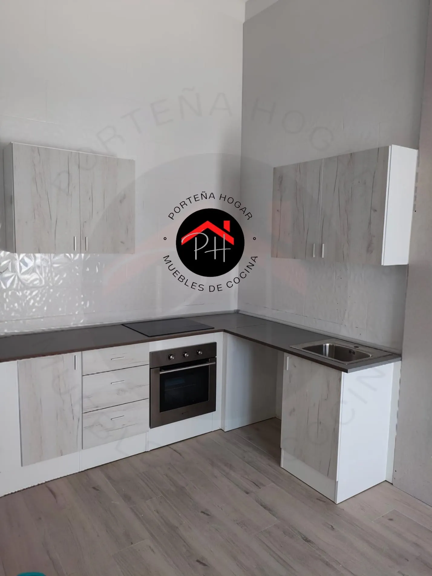 Cocina en L con puertas de acabado madera clara, base blanca, encimera gris, horno y cajones