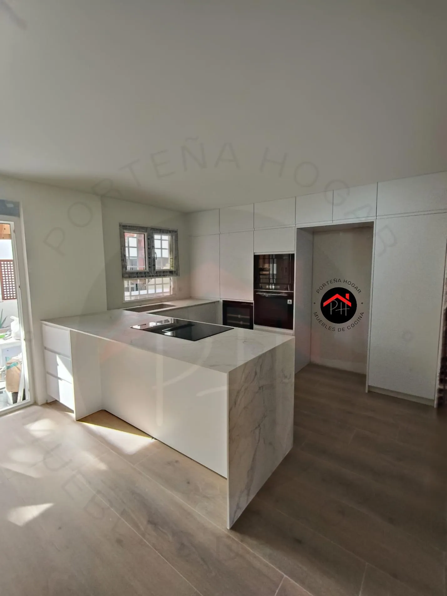 Cocina con península blanca, encimera veteada en cascada, placa negra y columnas de armarios