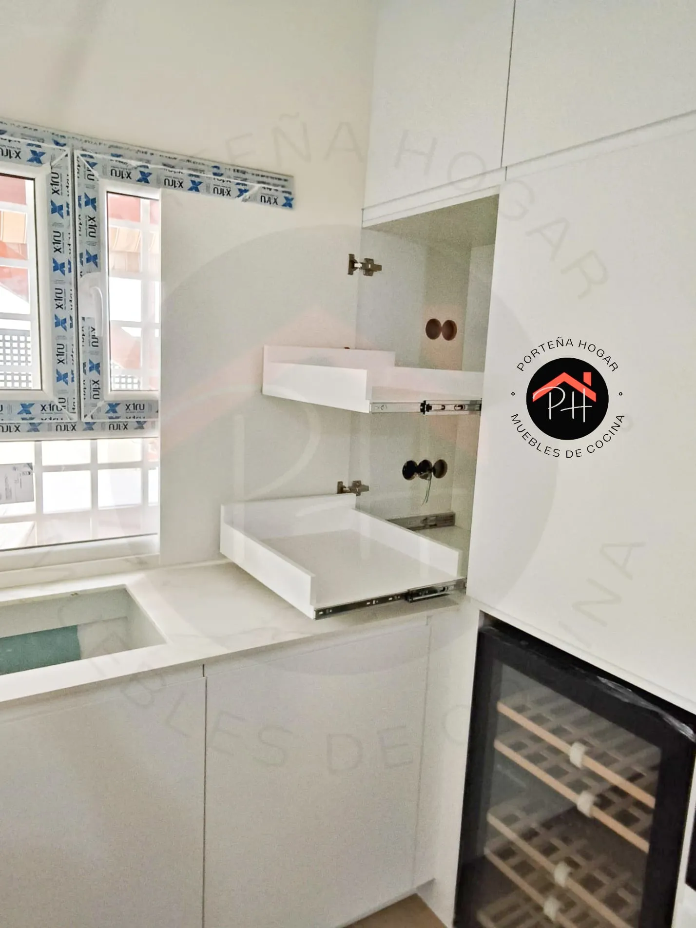 Detalle de una columna de cocina con dos baldas extraíbles blancas sobre guías, junto a un botellero